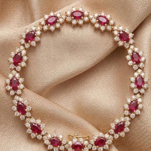 May include: A gold bracelet featuring oval-cut, deep red gemstones surrounded by small, sparkling white stones. The bracelet is set on a gold chain and has a secure clasp. The jewelry is displayed on a gold satin fabric.