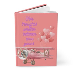 May include: Pink journal with the text "For thoughts written between time gones." The cover features a pink airplane and heart-shaped balloons. The journal has a spiral binding and white pages.