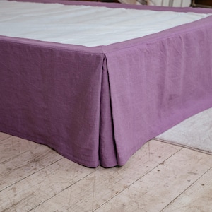 Może przedstawiać: Lawendowa spódnica do łóżka z plisowanym wzorem. Tkanina zwisa z ramy łóżka, zakrywając stelaż. Spódnica do łóżka wykonana jest z miękkiego, teksturowanego materiału i stoi na jasnej drewnianej podłodze.