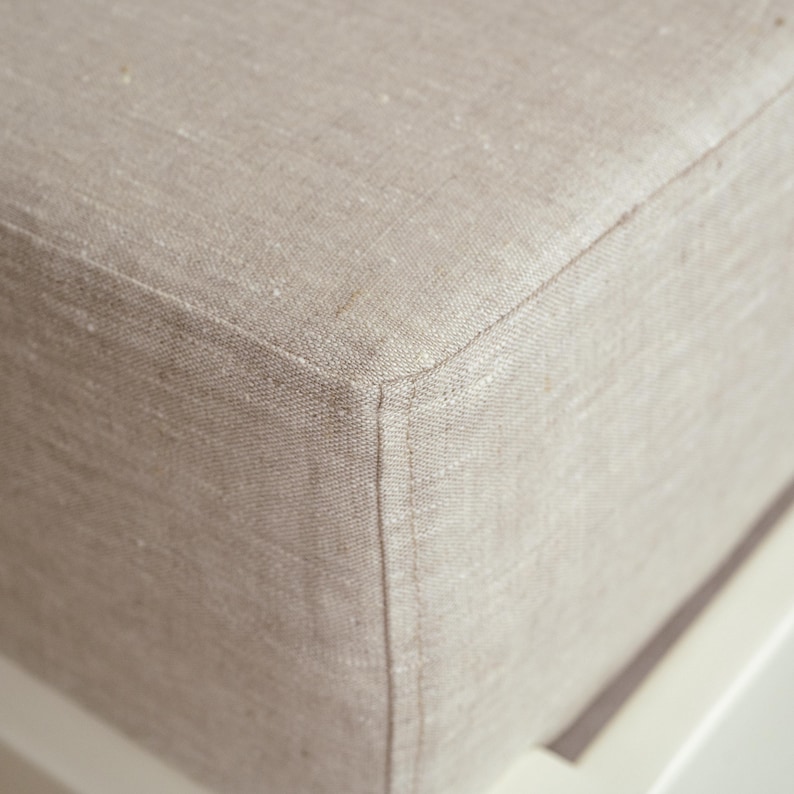 May include: Close-up of a beige linen fabric corner, showing the texture and stitching details. The fabric appears to be tightly woven, with a subtle sheen. The corner is neatly sewn, suggesting a high-quality construction.