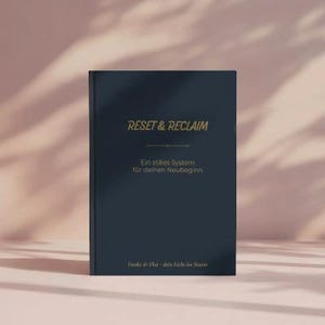 Op de afbeelding: Een marineblauw boek met de gouden tekst "RESET & RECLAIM" en Duitse tekst eronder. Het boek staat rechtop op een lichtroze ondergrond met schaduwen.