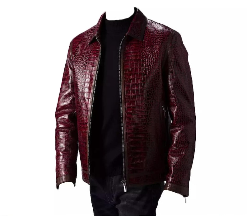 Puede incluir: Chaqueta de cuero burdeos con textura de piel de cocodrilo. La chaqueta tiene cierre de cremallera, cuello y mangas largas. La chaqueta se lleva sobre un cuello alto negro.