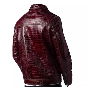 Puede incluir: Chaqueta de cuero burdeos con textura de piel de cocodrilo. La chaqueta tiene cuello alto, cierre de cremallera y ribetes marrones. La vista trasera muestra el dise&ntilde;o y los detalles de costura.