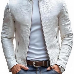 Puede incluir: Chaqueta de cuero blanca con un patrón de piel de cocodrilo texturizado, cierre de cremallera y cuello alto. La chaqueta se combina con una camiseta blanca y vaqueros azules. También se ven un cinturón marrón y un reloj.