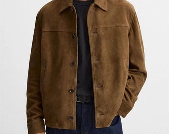 Peut inclure: Veste en daim marron avec une fermeture boutonnée et un col. La veste a un design classique et est associée à un t-shirt noir et un jean bleu foncé. La veste est de couleur marron moyen.