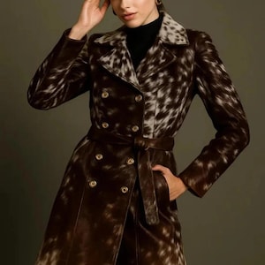 May include: A double-breasted brown and white patterned coat with a belt. The coat has a notched collar and gold buttons. The model is wearing a black turtleneck. The coat is knee-length.