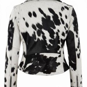May include: A jacket featuring a black and white cow print pattern throughout. The garment has a collared neckline, long sleeves with silver-toned metal zippers at the cuffs, and a fitted silhouette. The back view shows the full pattern.