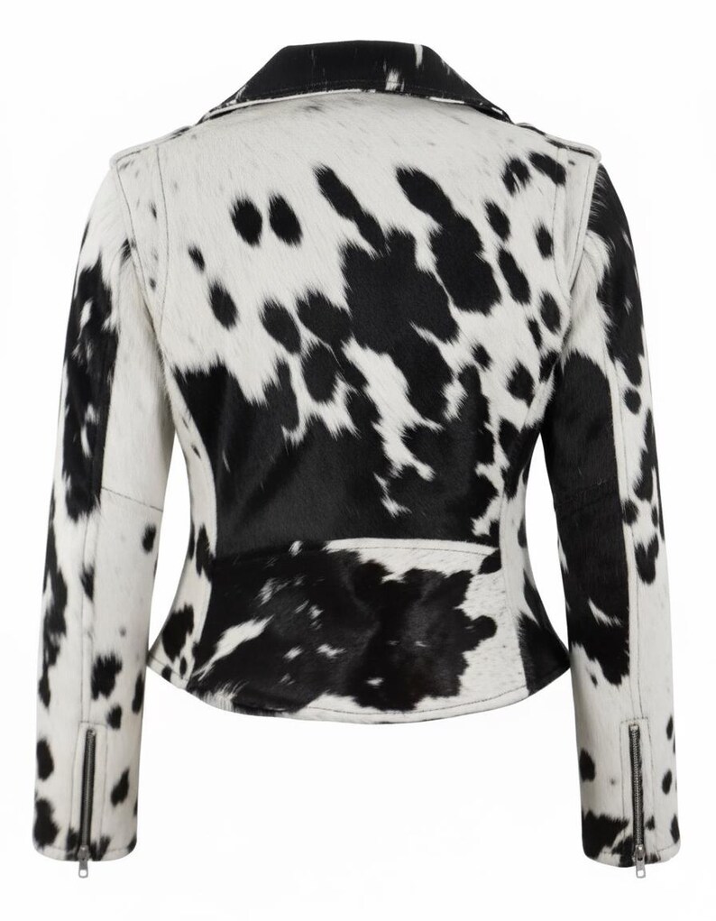 May include: A jacket featuring a black and white cow print pattern throughout. The garment has a collared neckline, long sleeves with silver-toned metal zippers at the cuffs, and a fitted silhouette. The back view shows the full pattern.