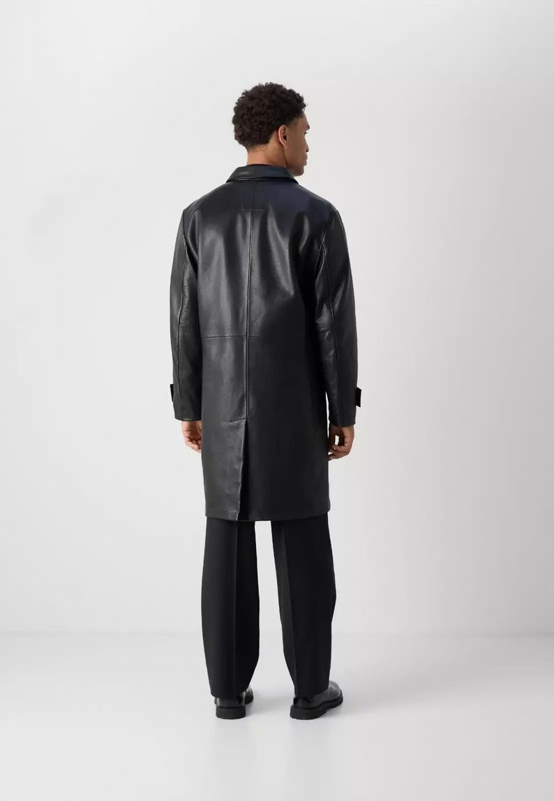 May include: A black leather coat with a classic design. The coat is long, reaching below the knees, and features a notched collar and button closures. The model is wearing black pants and shoes.