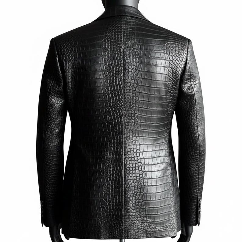 May include: Black blazer with a crocodile-effect texture. The jacket features a classic two-button closure and notched lapels. The blazer is displayed on a mannequin against a white backdrop.