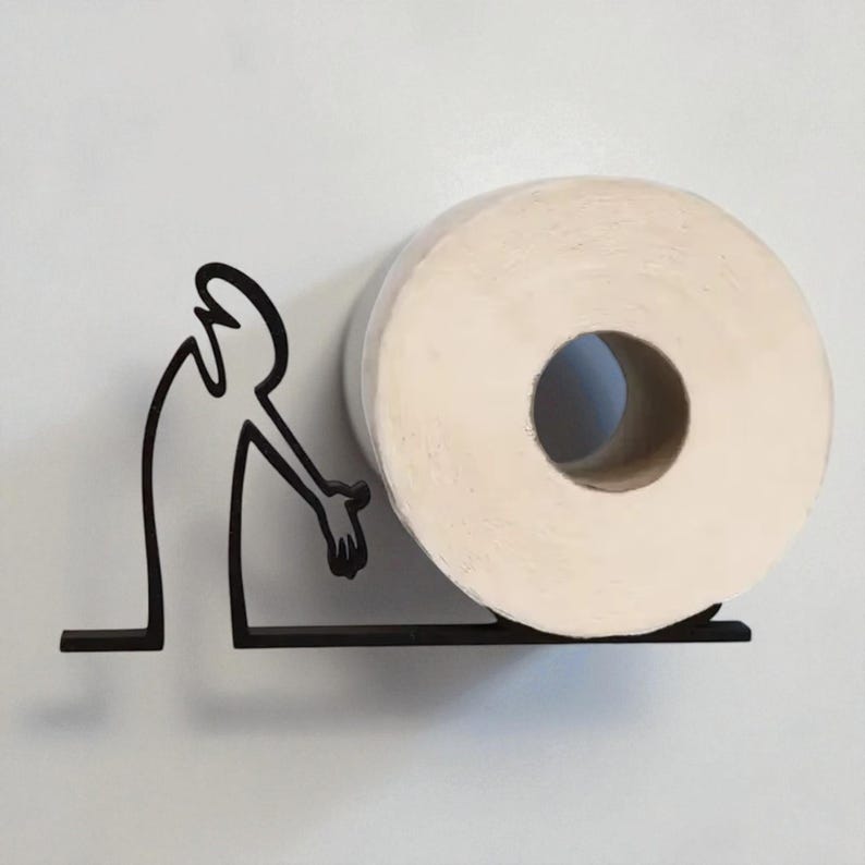May include: A black metal toilet paper holder featuring a stylized figure reaching towards a roll of white toilet paper. The holder is mounted on a white wall, creating a minimalist and modern bathroom accessory.