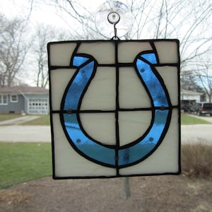 May include: A stained glass window hanging with a blue horseshoe design. The horseshoe is outlined in black and has white dots on it.