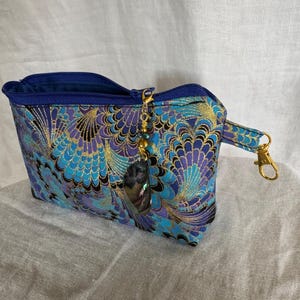 Zipper pouch in blues purple and gold and black with iridescent charm detachable zipper pull claw clasp on one of two side tabs blue lining