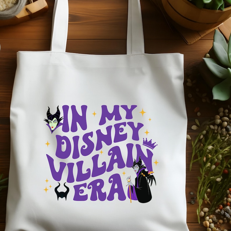 Puede incluir: Bolso tote blanco con el texto "IN MY DISNEY VILLAIN ERA" en morado, e ilustraciones de villanos de Disney. El bolso tiene dos asas y est&aacute; hecho de una tela resistente.