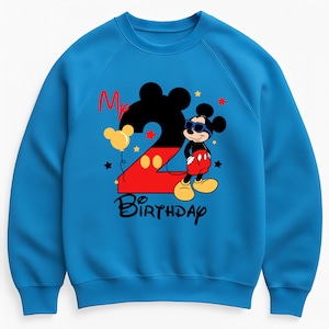 May include: A blue sweatshirt featuring a Mickey Mouse design for a second birthday. The design includes a large black number 2 with a red outline, Mickey Mouse wearing sunglasses, and the words "My Birthday". Yellow stars and a balloon complete the design.