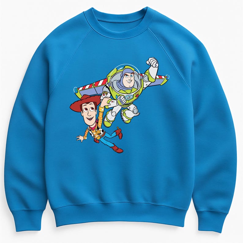 K&ouml;nnte beinhalten: Blauer Pullover mit einer Grafik von Woody und Buzz Lightyear aus Toy Story. Woody tr&auml;gt einen Cowboyhut, und Buzz ist in einem Raumanzug mit Fl&uuml;geln. Das Design ist in leuchtenden Farben auf einem einfarbigen blauen Hintergrund.
