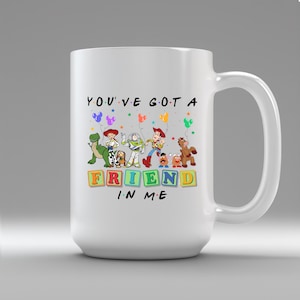May include: White ceramic mug featuring characters from the animated film Toy Story. The mug has the phrase "YOU'VE GOT A FRIEND IN ME" with colorful block letters and character illustrations. The mug has a large handle.