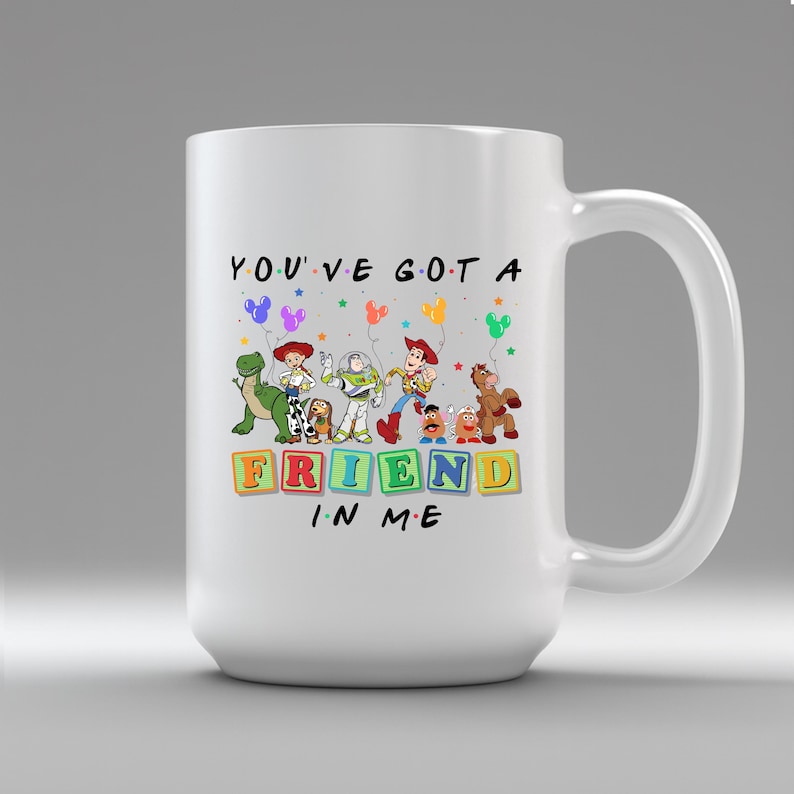 May include: White ceramic mug featuring characters from the animated film Toy Story. The mug has the phrase "YOU'VE GOT A FRIEND IN ME" with colorful block letters and character illustrations. The mug has a large handle.