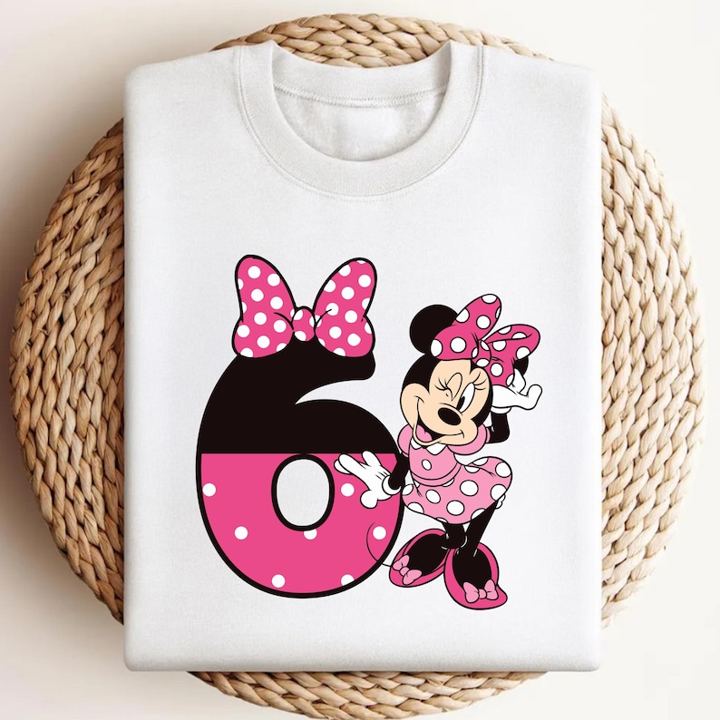 Puede incluir: Sudadera blanca con un gr&aacute;fico de Minnie Mouse y el n&uacute;mero 6. Minnie Mouse lleva un vestido y un lazo de lunares rosas. El n&uacute;mero 6 es negro y rosa con un lazo de lunares.