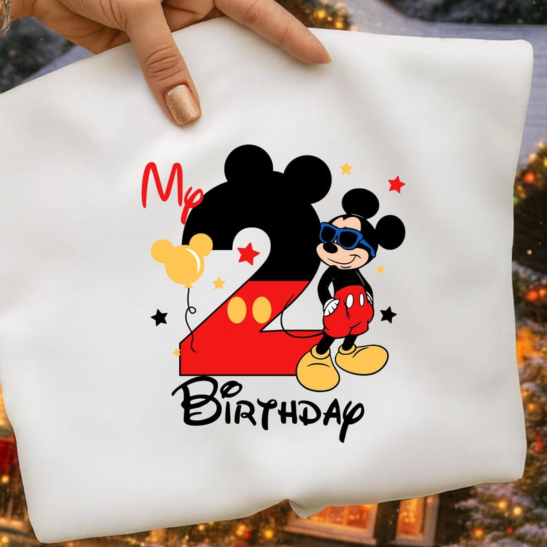 May include: White t-shirt featuring a colorful graphic of Mickey Mouse wearing sunglasses, with the number 2 in black and red, and the words "My Birthday". Includes yellow balloons and stars.