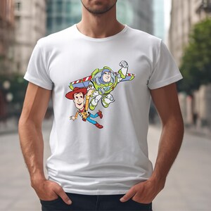 K&ouml;nnte beinhalten: Wei&szlig;es T-Shirt mit einem farbenfrohen Aufdruck von Woody und Buzz Lightyear aus Toy Story. Woody tr&auml;gt einen Cowboyhut und Buzz einen Raumanzug. Das Design befindet sich mittig auf dem Shirt.