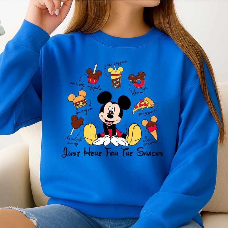 Puede incluir: Una sudadera azul real con un gr&aacute;fico de Mickey Mouse rodeado de ilustraciones de comida, incluyendo una hamburguesa, una rosquilla y helado. El texto "Just Here For The Snacks" est&aacute; debajo.