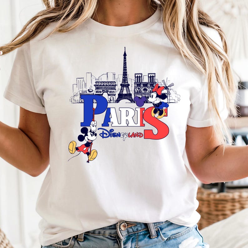 May include: White t-shirt with a graphic of the Paris skyline, including the Eiffel Tower, and the word "PARIS" in blue and red. Mickey and Minnie Mouse are also featured, along with the text "Disneyland".