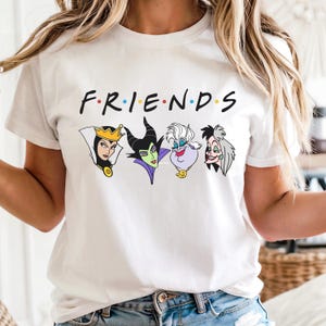 May include: White t-shirt featuring the word "FRIENDS" in a colorful font, with cartoon illustrations of four Disney villains below. The villains include the Evil Queen, Maleficent, Ursula, and Cruella de Vil.