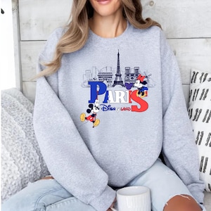 May include: A light grey sweatshirt with a graphic of the Paris skyline, the word "PARIS" in blue and red, and two Mickey Mouse characters. The text "Disneyland" is below the word "PARIS".