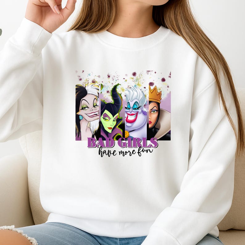 Puede incluir: Una sudadera blanca de manga larga con un estampado gr&aacute;fico de cuatro villanas animadas dispuestas en paneles verticales. Debajo de los personajes, el texto "BAD GIRLS have more fun" aparece en letras moradas y negras.