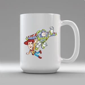 K&ouml;nnte beinhalten: Wei&szlig;er Keramikbecher mit einer farbenfrohen Grafik von Buzz Lightyear und Woody aus Toy Story. Buzz ist in einer Flugpose und Woody f&auml;llt. Der Becher hat einen gro&szlig;en Henkel. Geeignet f&uuml;r Hei&szlig;- und Kaltgetr&auml;nke.
