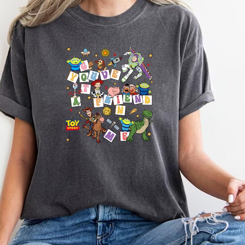 Puede incluir: Camiseta gris oscuro con un gr&aacute;fico colorido de Toy Story. El dise&ntilde;o incluye a Buzz Lightyear, Woody y otros personajes, con el texto "You've Got a Friend in Me". La camiseta tiene mangas cortas y un corte relajado.