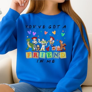 May include: A royal blue sweatshirt featuring a graphic of Toy Story characters. The phrase "YOU'VE GOT A FRIEND IN ME" is printed above the characters. Colorful balloons and the characters Woody, Buzz Lightyear, and others are depicted.
