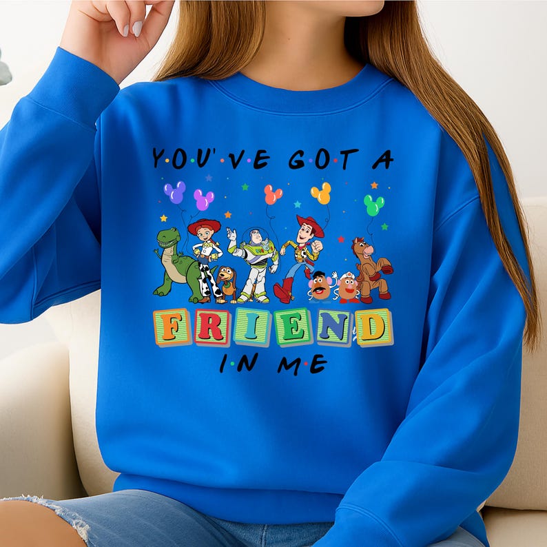 May include: A royal blue sweatshirt featuring a graphic of Toy Story characters. The phrase "YOU'VE GOT A FRIEND IN ME" is printed above the characters. Colorful balloons and the characters Woody, Buzz Lightyear, and others are depicted.
