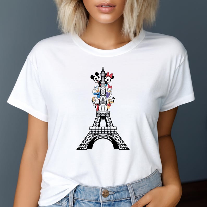 May include: White t-shirt with a black Eiffel Tower design and cartoon characters. The characters include Mickey Mouse, Minnie Mouse, Donald Duck, and Daisy Duck. The shirt has a crew neck.