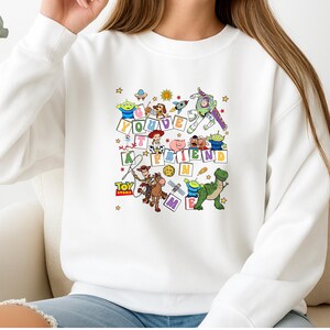 Puede incluir: Sudadera blanca con un gr&aacute;fico colorido de los personajes de Toy Story y la frase "You've Got a Friend in Me". El dise&ntilde;o incluye a Woody, Buzz Lightyear y otros personajes de la pel&iacute;cula animada, con estrellas y otros elementos decorativos.