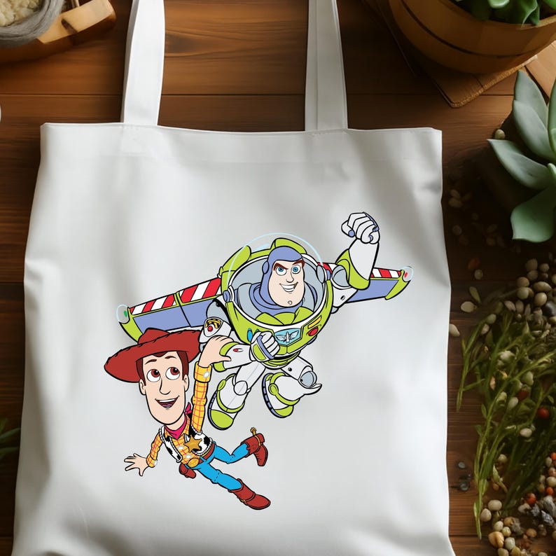 K&ouml;nnte beinhalten: Wei&szlig;e Tragetasche mit einer Grafik von Buzz Lightyear und Woody aus Toy Story. Buzz Lightyear tr&auml;gt einen gr&uuml;nen und wei&szlig;en Raumanzug mit Fl&uuml;geln, und Woody tr&auml;gt einen Cowboyhut und eine Weste. Die Tasche hat zwei wei&szlig;e Griffe.