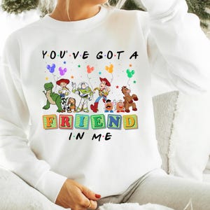 May include: White sweatshirt featuring a colorful graphic of Toy Story characters and the text "YOU'VE GOT A FRIEND IN ME". The design includes Woody, Buzz Lightyear, and other characters from the animated film.