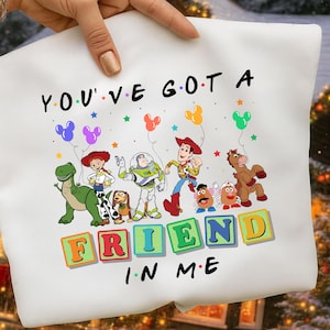 May include: White sweatshirt featuring a colorful graphic of Toy Story characters with the text "YOU'VE GOT A FRIEND IN ME". The design includes Woody, Buzz Lightyear, and other characters from the movie.