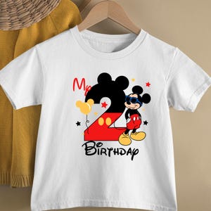 May include: White t-shirt featuring a Mickey Mouse design for a second birthday. The design includes a large number 2, Mickey Mouse wearing sunglasses, balloons, stars, and the words "My Birthday".
