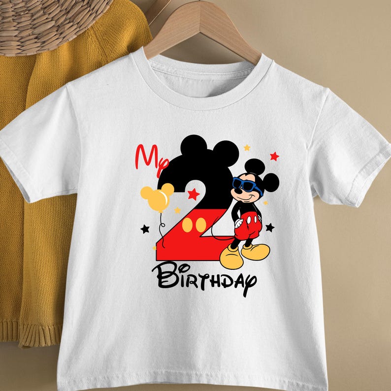 May include: White t-shirt featuring a Mickey Mouse design for a second birthday. The design includes a large number 2, Mickey Mouse wearing sunglasses, balloons, stars, and the words "My Birthday".