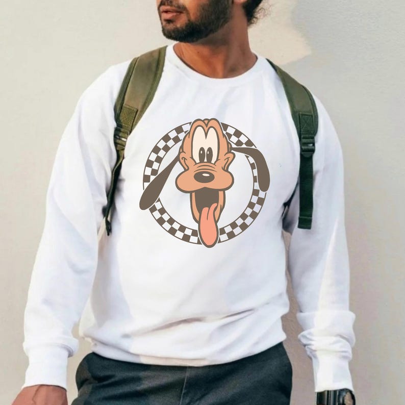 Op de afbeelding: Witte longsleeve sweatshirt met een cartoonafbeelding van Pluto, de Disney-hond. De afbeelding toont Pluto's gezicht met zijn tong uit, omgeven door een geblokte cirkel. Een casual sweatshirt.