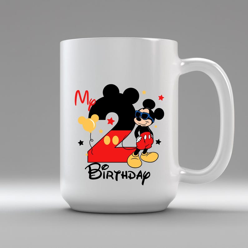 May include: White ceramic mug featuring a colorful Mickey Mouse design. The design includes a large number 2, Mickey Mouse wearing sunglasses, and the words "My Birthday". The mug is a fun and festive item.