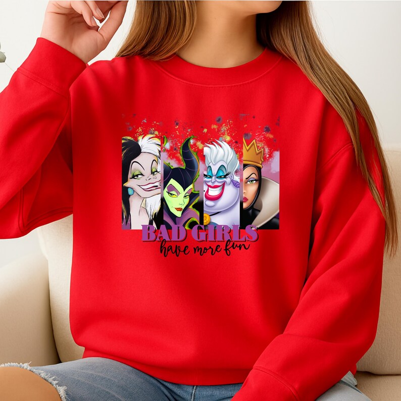 Puede incluir: Una sudadera roja de manga larga con un estampado gr&aacute;fico de cuatro villanas animadas dispuestas en paneles verticales. Debajo de los personajes, el texto dice "BAD GIRLS have more fun" en una combinaci&oacute;n de letras moradas y cursiva negra.
