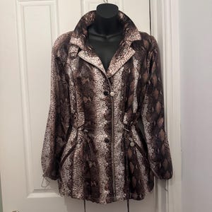 Peut inclure: Une veste à manches longues avec un motif imprimé peau de serpent dans des tons marron, noir et blanc. La veste présente un col montant, une fermeture éclair frontale intégrale, des détails argentés et des cordons de serrage à la taille.