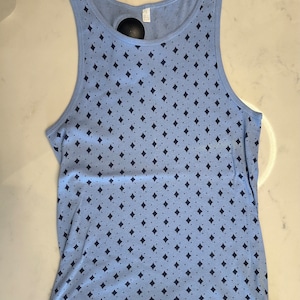 Peut inclure: Débardeur bleu clair avec un motif répétitif de losanges et de points bleu marine. Le haut sans manches a une encolure dégagée et est fait d'une matière douce et légère. Une étiquette noire est attachée près de l'encolure.