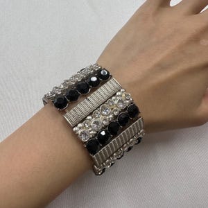 May include: A silver-toned bracelet set with multiple bands. The bands feature alternating rows of black and clear gemstones. The bracelet is worn on a wrist, showcasing the jewelry's design and sparkle. The bracelet is a fashion accessory.