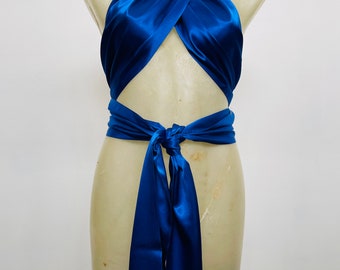 May include: A royal blue satin halter top displayed on a mannequin. The top features a wrap-around design with a knot at the waist and long, flowing ties. The fabric has a lustrous sheen.