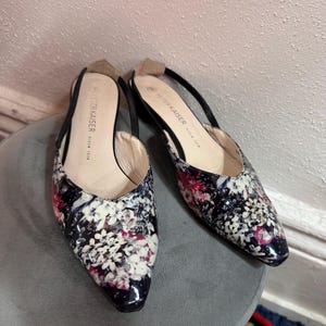 以下が含まれることがあります： ネイビー、白、ピンクの花柄のポインテッドトゥスリングバックフラットのペア。靴は黒いストラップで、「PETER KAISER」のブランド名がインソールに見えます。