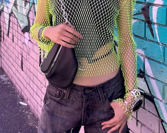 May include: A woman wearing a lime green mesh top with a black tank top underneath, ripped denim shorts, and a black chain strap bag.